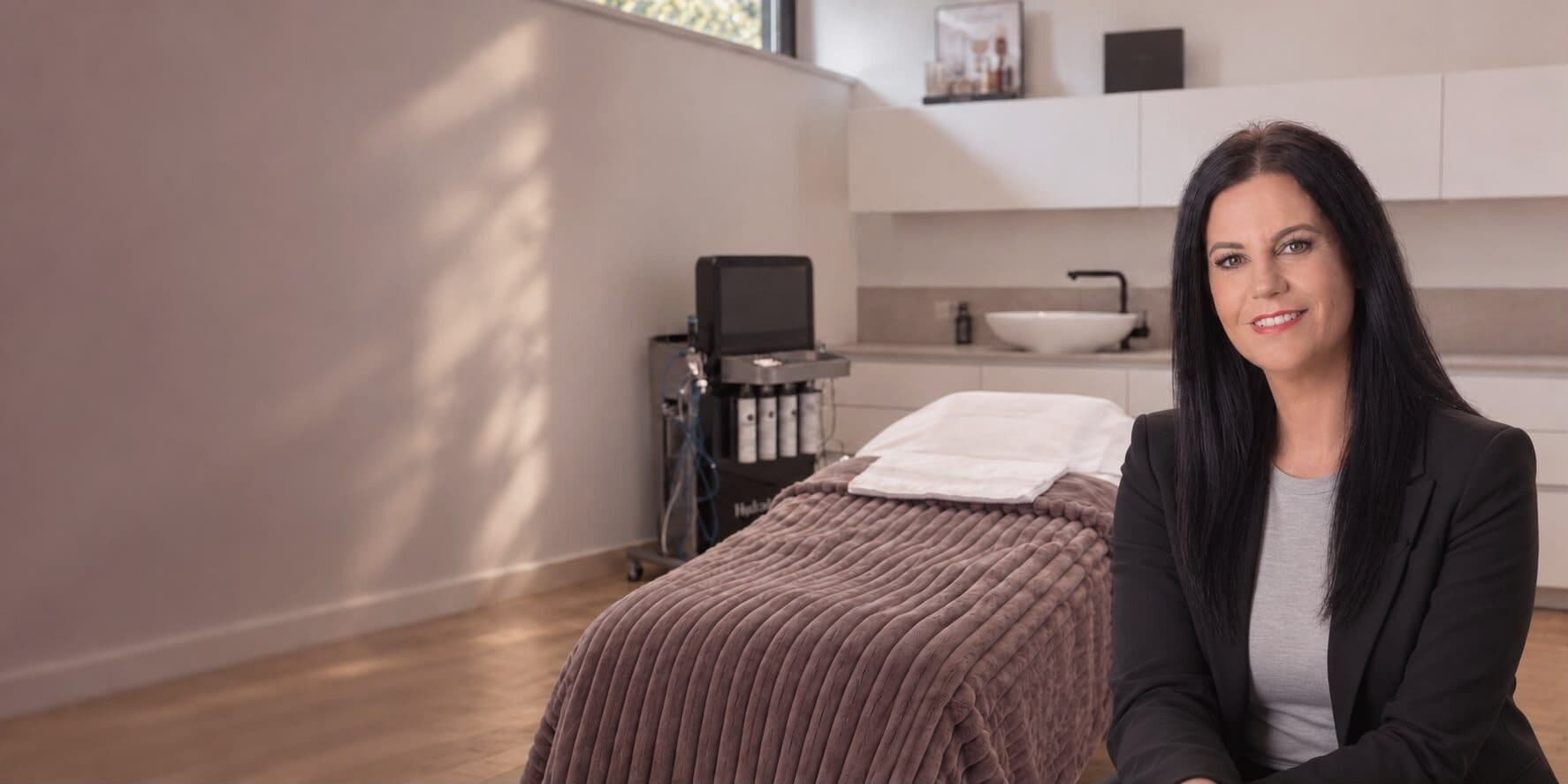 Pamela Paulini, Inhaberin des Beautyloft, in ihrem hellen Behandlungsraum; dahinter die Liege mit Mauve-Decke und das HydraFacial-Gerät