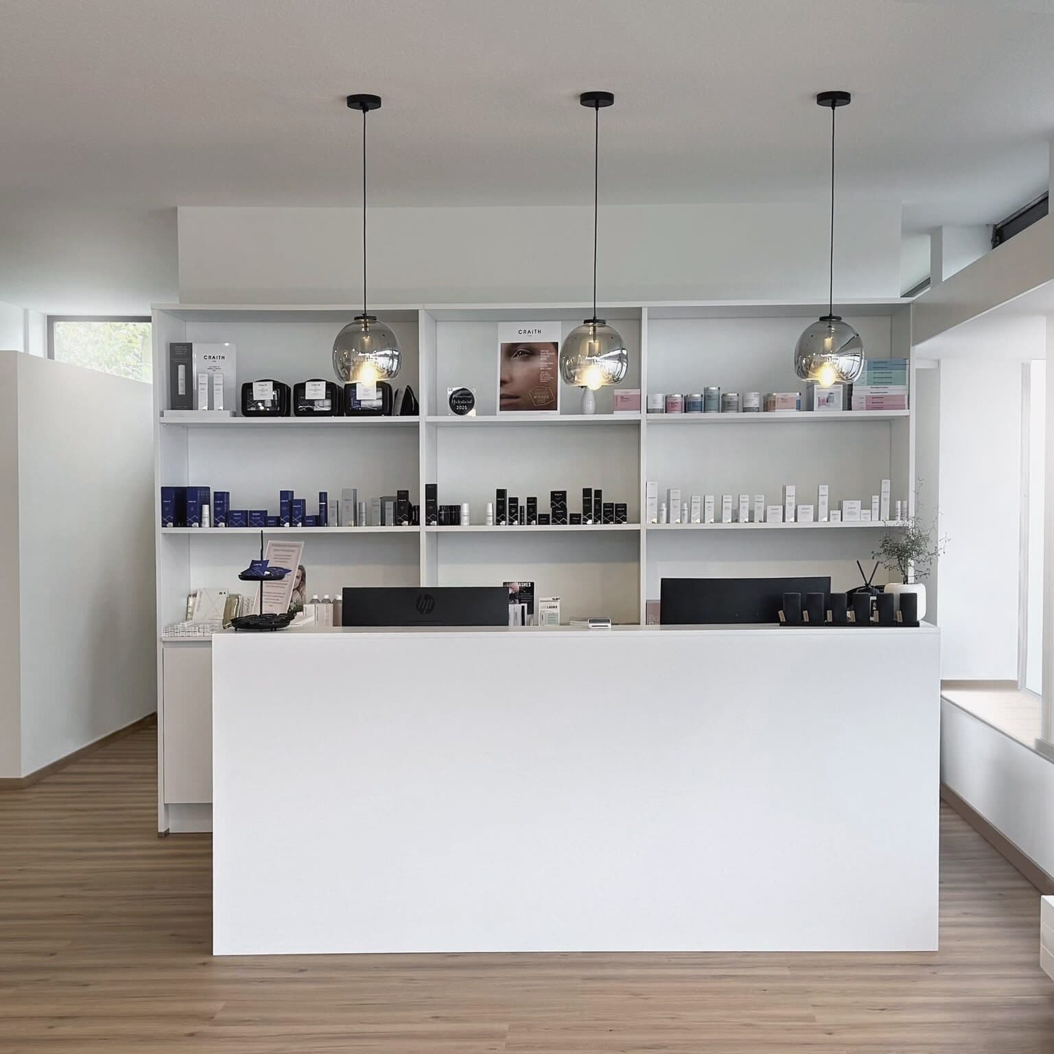 Empfang im Beautyloft: weisse Theke, Regal mit Pflegeprodukten und drei gläserne Pendelleuchten
