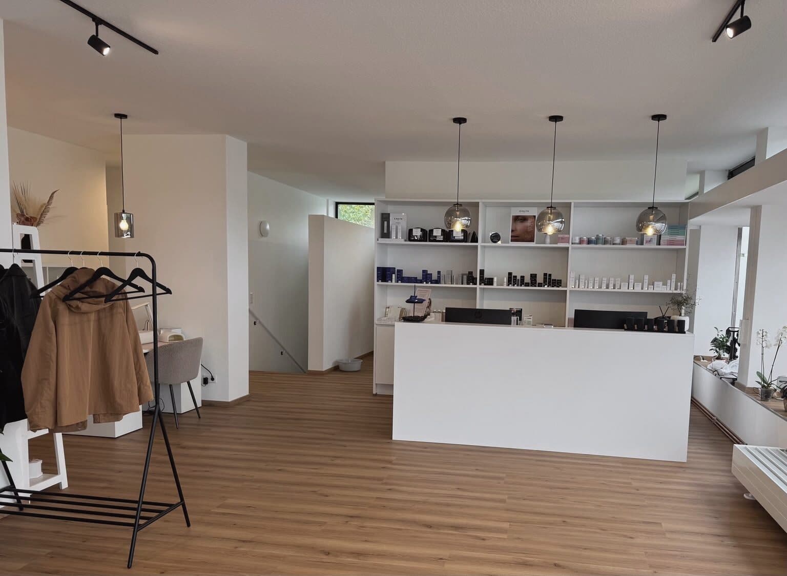 Blick in den hellen Empfangsbereich des Beautyloft mit Theke, Produktregal und Pendelleuchten