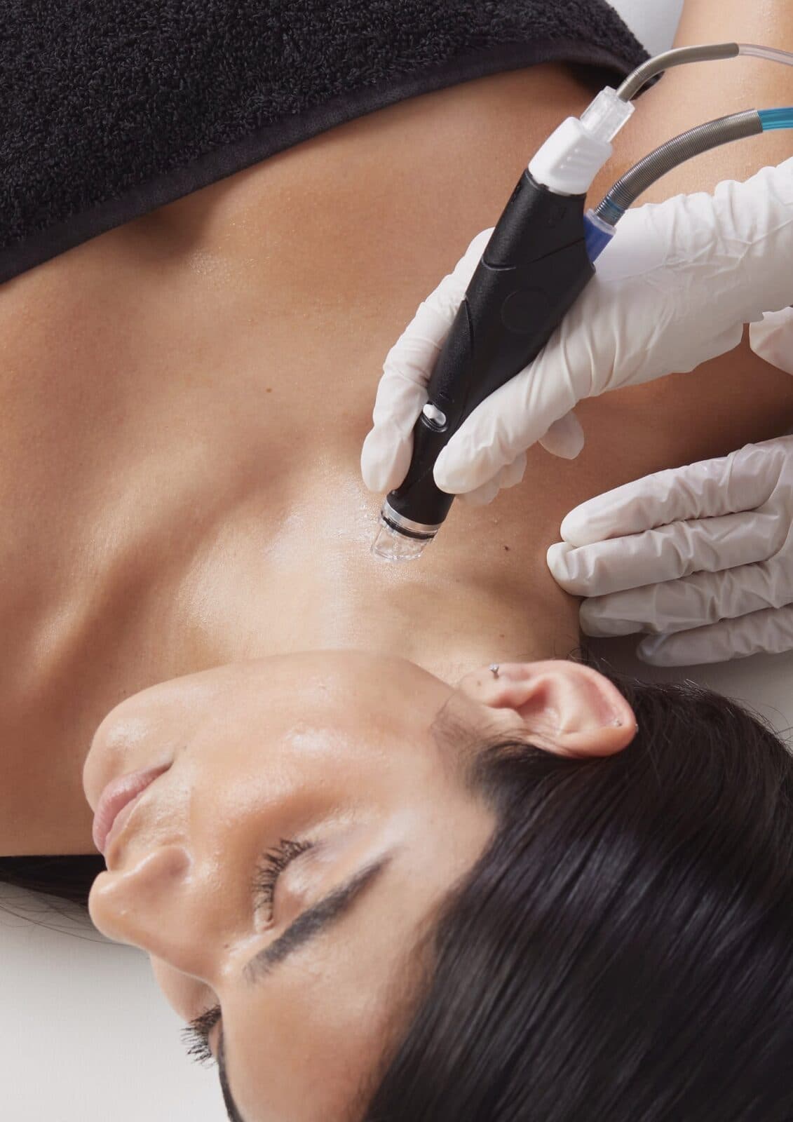 Handstück eines HydraFacial-Geräts wird seitlich am Hals geführt, Hände in weissen Handschuhen