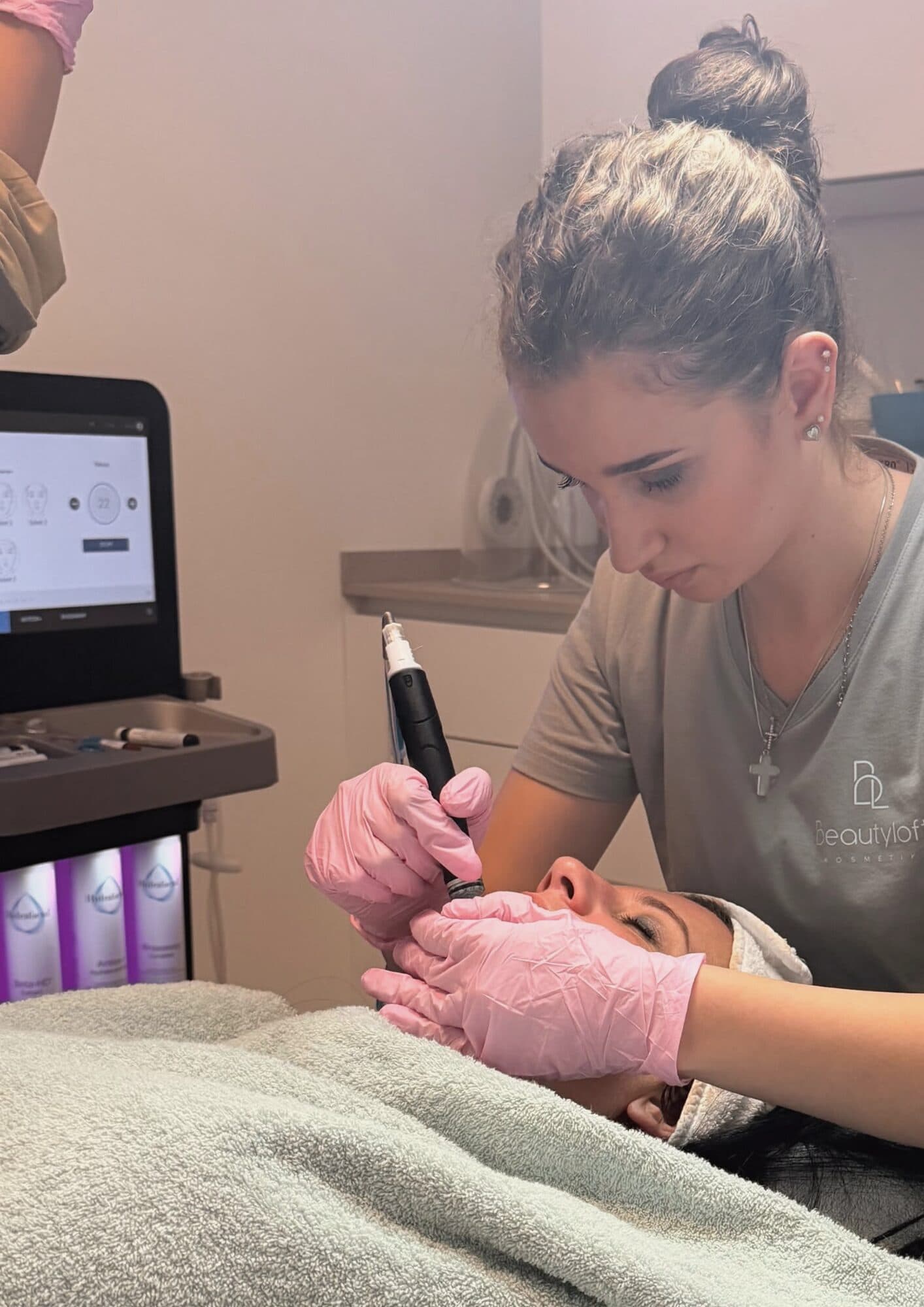Mitarbeiterin im Beautyloft-Shirt bei einer Gesichtsbehandlung, dahinter das HydraFacial-Gerät